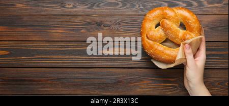 Femme avec de savoureux bretzel fraîchement cuit à table en bois, vue de dessus avec espace pour le texte. Bannière Banque D'Images