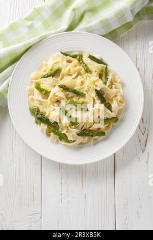 Pâtes de fettuccine aux asperges, citron dans une sauce crémeuse au fromage en gros plan dans une assiette sur la table. Vue verticale du dessus Banque D'Images