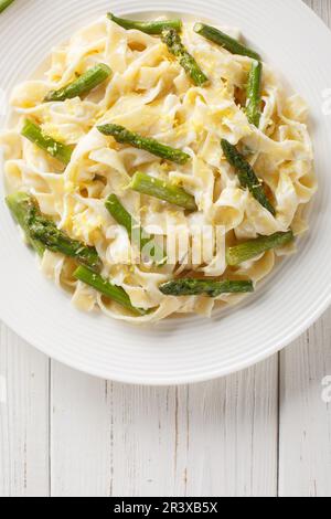 Pâtes avec asperges frites, zeste de citron dans une sauce crémeuse au parmesan, dans une assiette sur la table. Vue verticale du dessus Banque D'Images