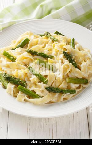 Pâtes de fettuccine aux asperges, citron dans une sauce crémeuse au fromage en gros plan dans une assiette sur la table. Verticale Banque D'Images