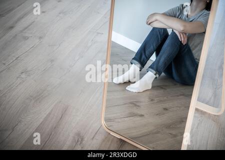Réflexion en mirule d'une femme triste assise sur un sol seul dans une pièce vide, désespoir et concept solitaire avec espace de copie, tonne grise Banque D'Images