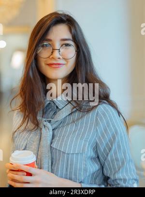 Une jeune femme asiatique au café tient une boisson chaude dans une tasse de papier Banque D'Images