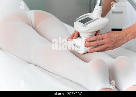 Femme en costume blanc spécial recevant un massage anti cellulite pour les jambes dans un salon de spa. GPL et traitement de contour du corps en clinique Banque D'Images