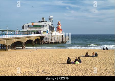Personnes assises sur la plage de Bournemouth le jour du printemps avec Bournemouth Pier, Angleterre Royaume-Uni Banque D'Images