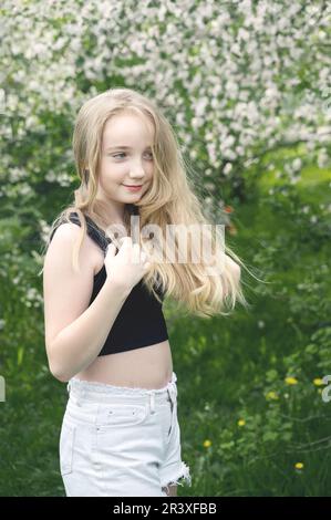 une belle fille de 13-15 ans sourit dans le jardin de printemps, luttant avec la dépression de printemps et appréciant les fleurs. Une fille heureuse est souriante dans na Banque D'Images