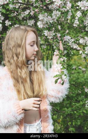 une belle fille de 13-15 ans sourit dans le jardin de printemps, luttant avec la dépression de printemps et appréciant les fleurs. Une fille heureuse est souriante dans na Banque D'Images