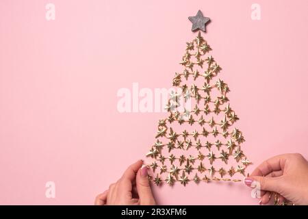 Vue de dessus des mains de femmes décorant l'arbre de Noël doré sur fond rose. Pose à plat Banque D'Images