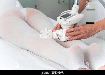 Femme en costume blanc spécial recevant un massage anti cellulite pour les jambes dans un salon de spa. GPL et traitement de contour du corps en clinique Banque D'Images