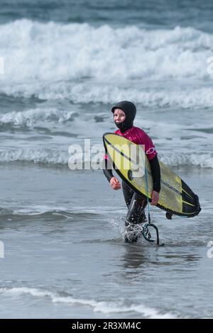 Un jeune surfeur mâle transportant son surf et marchant hors de la mer après avoir conté à la compétition de surf RIP Curl Grom Search au Fistral au ne Banque D'Images