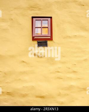Petite fenêtre marron sur le grand mur de maçonnerie jaune Banque D'Images