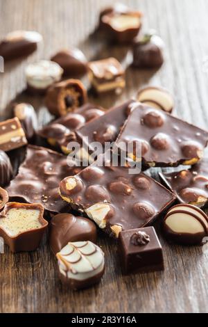 Barres de chocolat cassées avec des noix et des pralines sur la table en bois. Banque D'Images