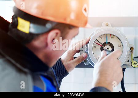 Le monteur d'instruments règle et diagnostique le manomètre ou le manomètre dans les installations industrielles intérieures. Vue arrière en gros plan. Un vrai travailleur au travail. Banque D'Images