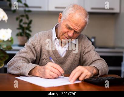 un aîné écrit une lettre sur papier à la maison Banque D'Images