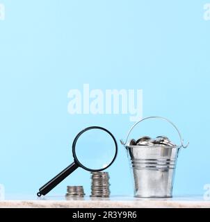 Une pile de pièces de monnaie en métal et une loupe en plastique sur fond bleu. Le concept de l'augmentation des impôts, des subventions Banque D'Images