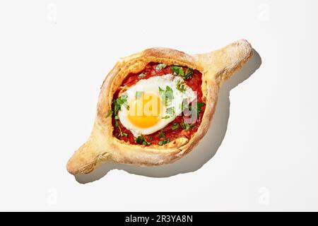 Adjarian khachuri sur fond blanc. Une version non conventionnelle de la cuisine géorgienne, bateau à pâte avec fromage, tomates, herbes Banque D'Images