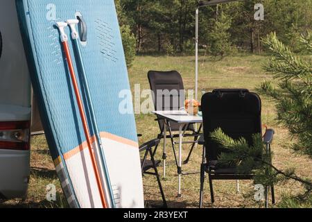 Les planches d'aviron gonflables Sup se tiennent près du camping-car gonflé dans la nature pendant la journée. Banque D'Images