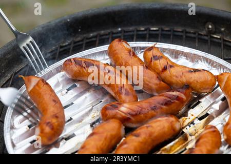 Les mains d'une personne tenant deux fourchettes modifient la position de la saucisse sur la grille du gril de jardin. Photo prise dans des conditions d'éclairage naturel Banque D'Images