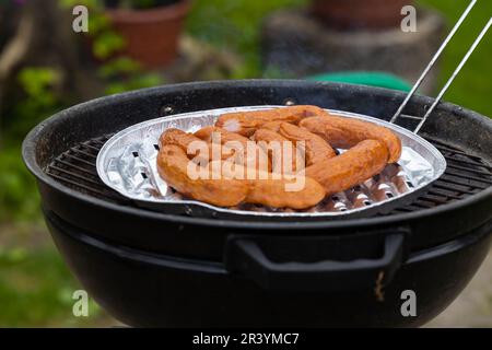 Saucisses fraîches sur une grille dans le jardin. Saucisses disposées sur un plateau en aluminium Photo prise dans des conditions d'éclairage naturel. Banque D'Images