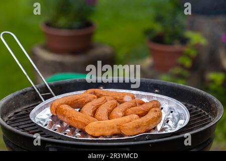 Saucisses fraîches sur une grille dans le jardin. Saucisses disposées sur un plateau en aluminium Photo prise dans des conditions d'éclairage naturel. Banque D'Images