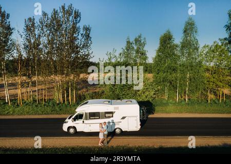 Un couple est debout sur la route près de leur motorhome à l'aube. Banque D'Images