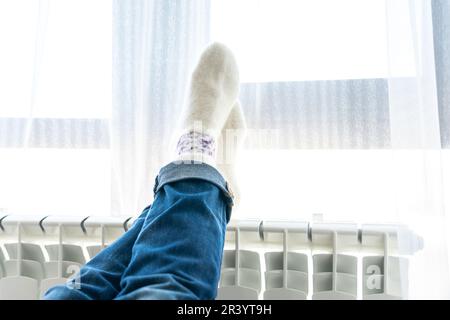 Femme portant des chaussettes en laine avec les pieds sur le radiateur Banque D'Images