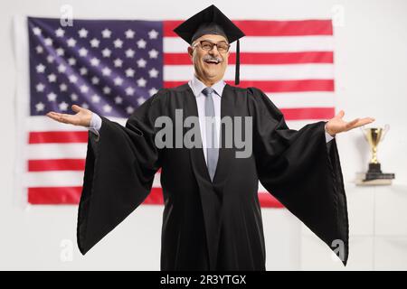 Homme mûr gai portant une robe de graduation devant le drapeau des États-Unis Banque D'Images