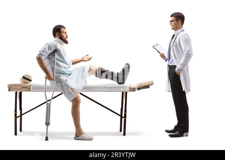 Patient avec une chaussure orthopédique et un col de cou assis sur une table de thérapie et parlant à un thérapeute isolé sur fond blanc Banque D'Images