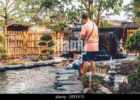 KANCHANABURI -THAÏLANDE, 30 MARS 2023 : touristes non identifiés viennent visiter et nourrir koi ou carpe fantaisie dans un petit étang avec beau jardin décoré Banque D'Images