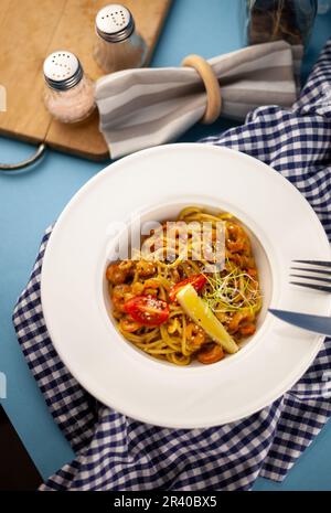 Spaghetti aux crevettes, citron et micro-vert. Déjeuner dans un plat blanc profond, gros plan. Pâtes avec fruits de mer, tomates et salade. Banque D'Images