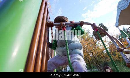 Petit garçon s'exerçant à l'extérieur tenant dans la barre métallique à la structure de l'aire de jeux. Enfant actif être actif à l'extérieur. Style de vie de l'enfance Banque D'Images