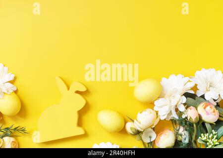 Composition de Pâques avec œufs colorés, lapin en bois et fleurs de printemps sur fond jaune. Vue de dessus. Copier l'espace. Banque D'Images