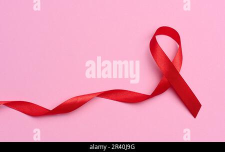 Un ruban rouge en soie sous la forme d'un arc sur fond rose, un symbole de la lutte contre le sida et un signe de solidarité et de sup Banque D'Images