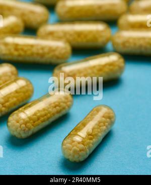 Capsules médicales transparentes avec granules jaunes à l'intérieur sur fond bleu, comprimés pour le traitement, vitamines Banque D'Images