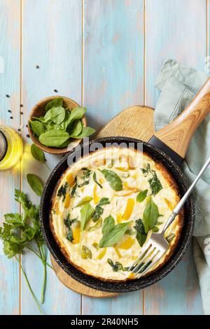 Frittata saine ou omelette farcie dans une casserole sur fond rustique en bois. Omelette italienne aux épinards bio et au poivron. Banque D'Images