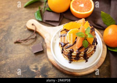Fêtez la fête du Pancake, petit déjeuner américain sain. Délicieuses crêpes aux bananes avec chocolat et oranges rouges sur table rustique. Banque D'Images