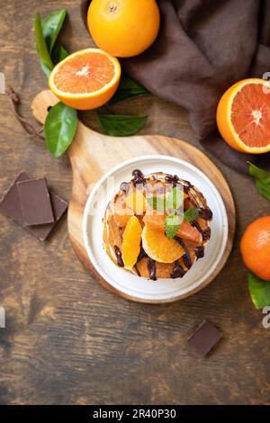 Fêtez la fête du Pancake, petit déjeuner américain sain. Délicieuses crêpes aux bananes avec chocolat et oranges rouges sur table rustique. Banque D'Images