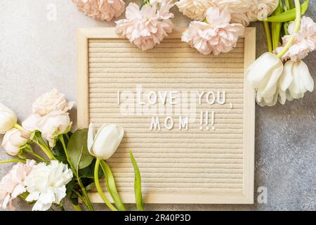 Bonne fête des mères. Lettre J'AIME MOM sur le carton et belles fleurs de printemps sur fond clair. Fête des femmes, mariage, papillon Banque D'Images