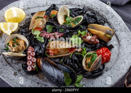 Les fruits de mer. fehttuchini fettuccine noir Les pâtes noires avec des calmars, poulpes les palourdes, les moules sur la plaque de pierre. Plat gastronomique Banque D'Images