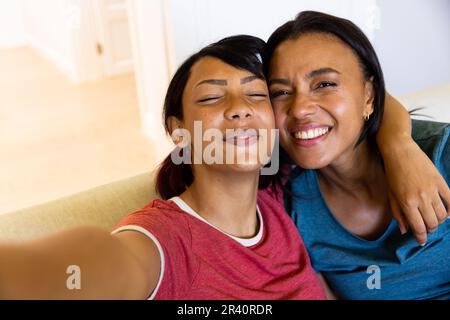Portrait de sœurs biraciales heureuses regardant l'appareil photo, prenant le selfie, souriant et enveloppant Banque D'Images