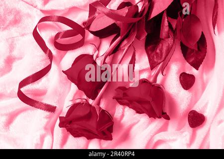 Saint Valentin surprise. Roses rouges et coeurs sur le lit. Plan d'agencement avec vue de dessus. Couleur tendance de l'année 2023 - Viva Magenta. Banque D'Images