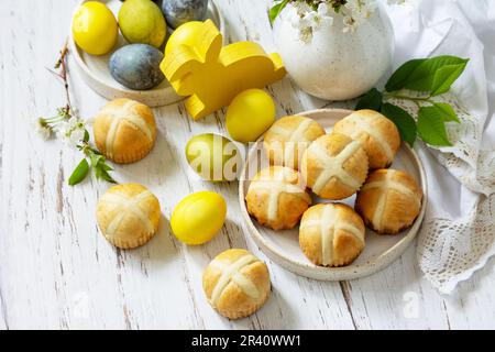 Concept de la nourriture festive joyeuses Pâques. Petits pains traditionnels de Pâques faits maison à la croix chaude avec raisins secs et œufs de pâques colorés naturels sur un Banque D'Images