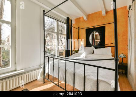 un lit dans une chambre avec des murs orange et des draps blancs sur le lit, cadre en métal noir autour de la tête de lit Banque D'Images