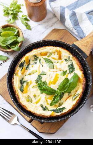 Omelette aux épinards et au fromage. Frittata fait d'oeufs, de paprika et d'épinards dans une poêle sur un comptoir en marbre. Banque D'Images