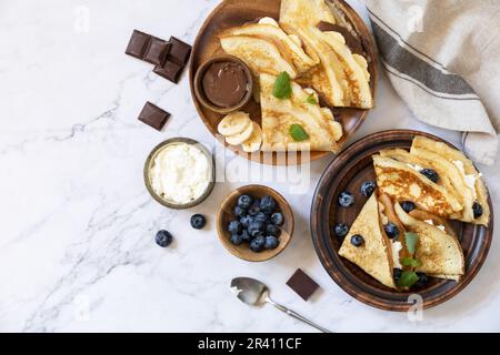Fête du Pancake, petit déjeuner sain. Délicieuses crêpes maison au caramel au chocolat, aux bananes, aux bleuets et au ricott Banque D'Images