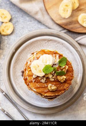 Fêtez le Pancake Day, petit déjeuner américain fait maison. Crêpes sans gluten à la banane avec noix et caramel sur table en pierre. Vue Banque D'Images