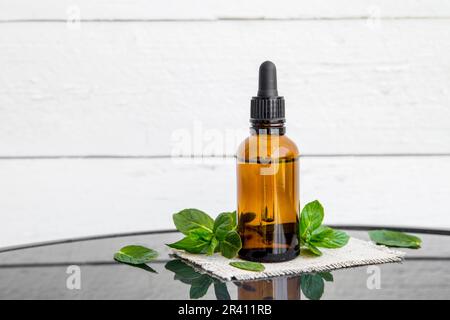 Bouteille brune d'huile essentielle de menthe poivrée ou infusion dans une bouteille de pipette médicale avec des branches de menthe poivrée fraîche pour la décoration sur une table en verre. Banque D'Images