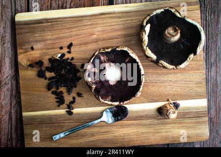 Nettoyage et endirage d'une paire de chapeaux de champignons Portobello : raclage des branchies des chapeaux de champignons crus sur une planche à découper en bois Banque D'Images