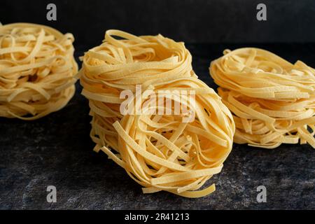 Le Tagliatelle empilé niche sur un arrière-plan sombre : vues de côté et de dessus des nids de pâtes séchées empilés sur le dessus de l'eachautre Banque D'Images