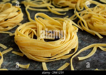 Tagliatelle nids de pâtes entourés de nouilles brisées éparses : vue en gros plan des nids de pâtes séchées entourés de nouilles cassées Banque D'Images
