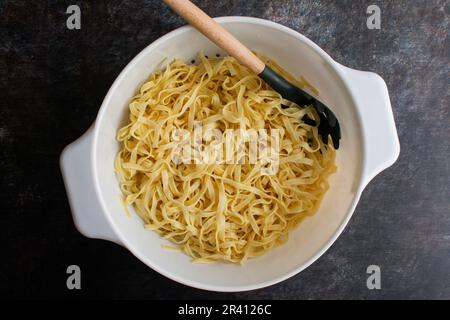 Pâtes Tagliatelle cuites dans une grande passoire avec une cuillère à pâtes : nouilles fraîchement cuites et égouttées dans une grande passoire avec une fourchette à pâtes Banque D'Images